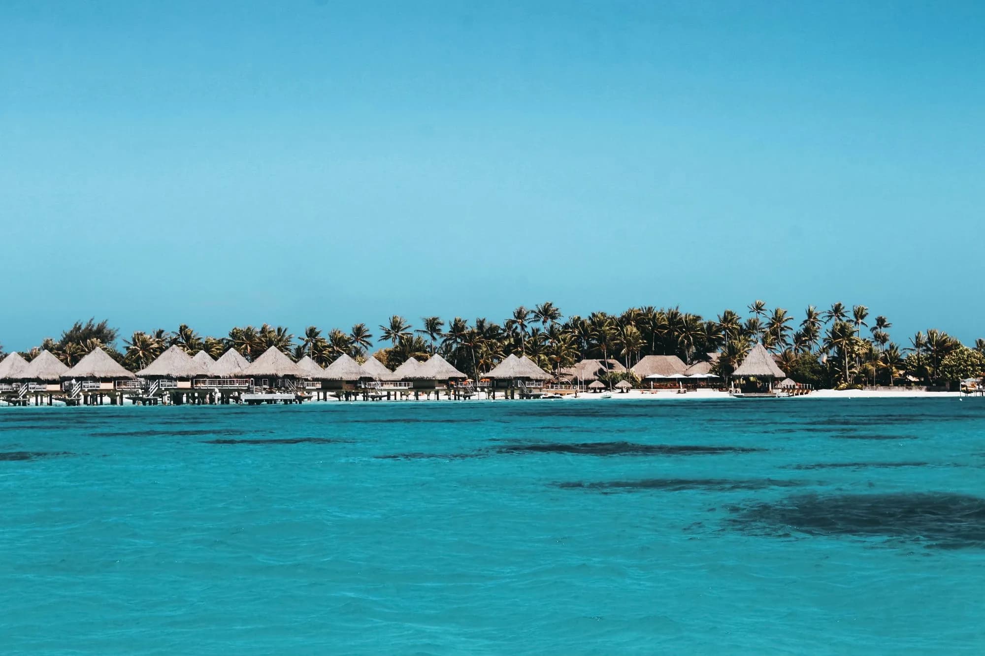 Thatched bungalows lining a turquoise lagoon in French Polynesia