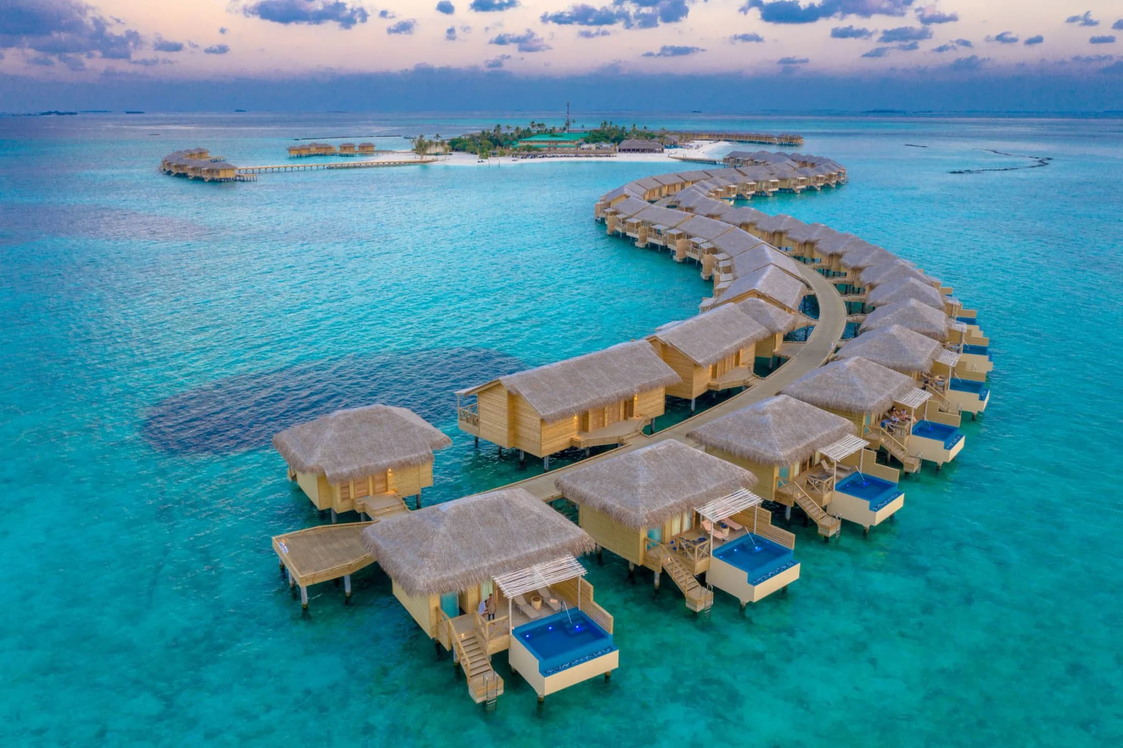 Aerial view of overwater villas with private pools curving across a turquoise Maldives lagoon